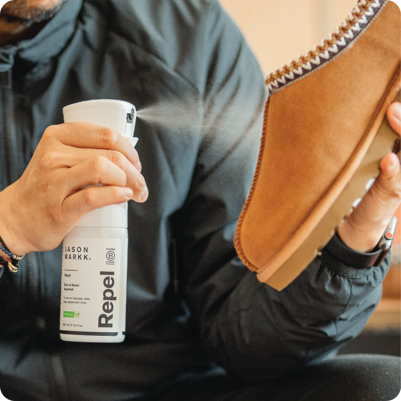 Person holding a bottle of Repel spraying it on a brown shoe.
