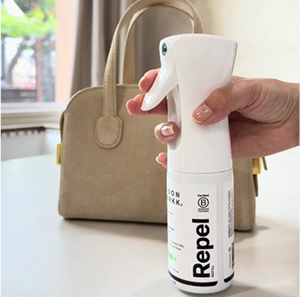 Hand holding Repel with a beige handbag in the background.