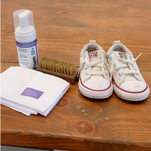 White sneakers with red soles on a wooden surface, accompanied by RTU Foam, Delicates Brush, and Microfiber Towel.